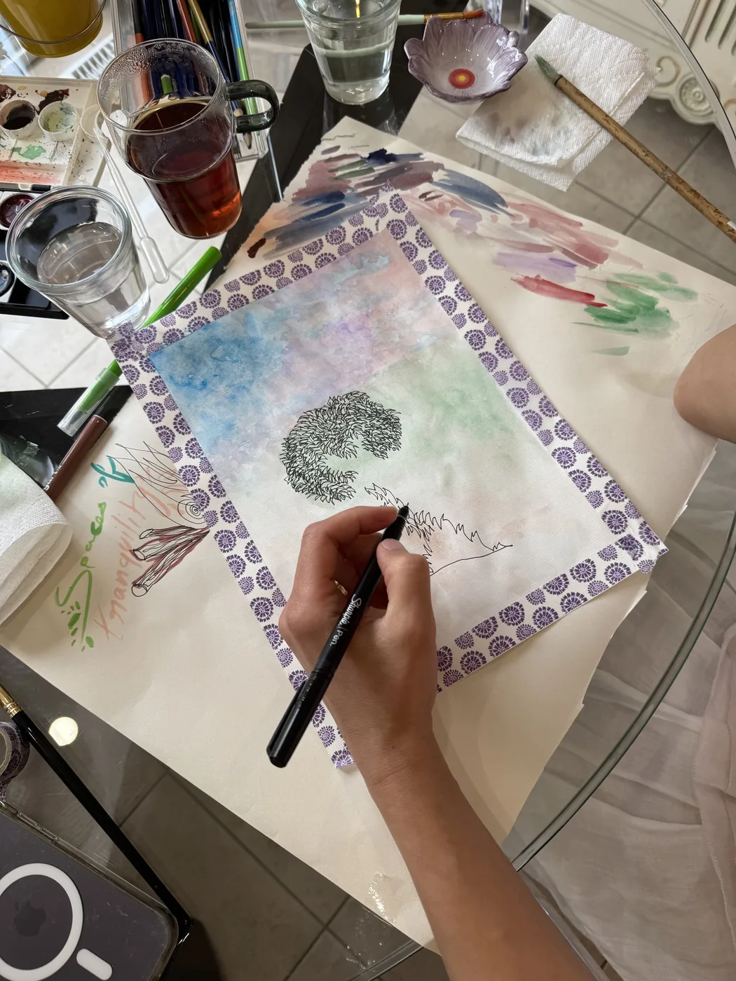 Adult hand inking a tree inside a patterned border