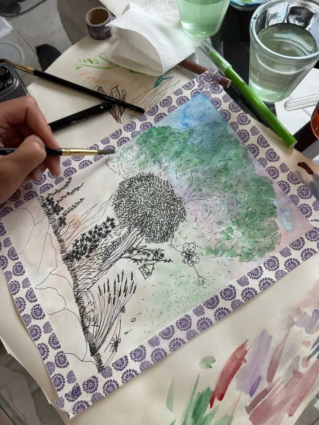 Adult hand inking a tree over a watercolour wash
