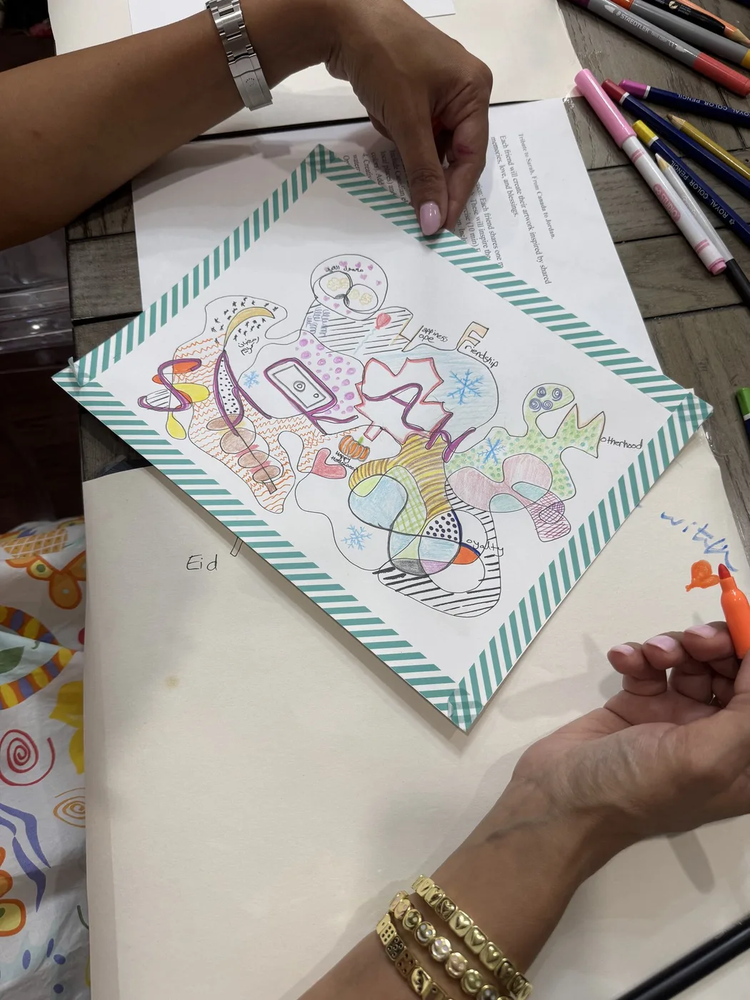 Adult hands with bracelets colouring a doodle tribute