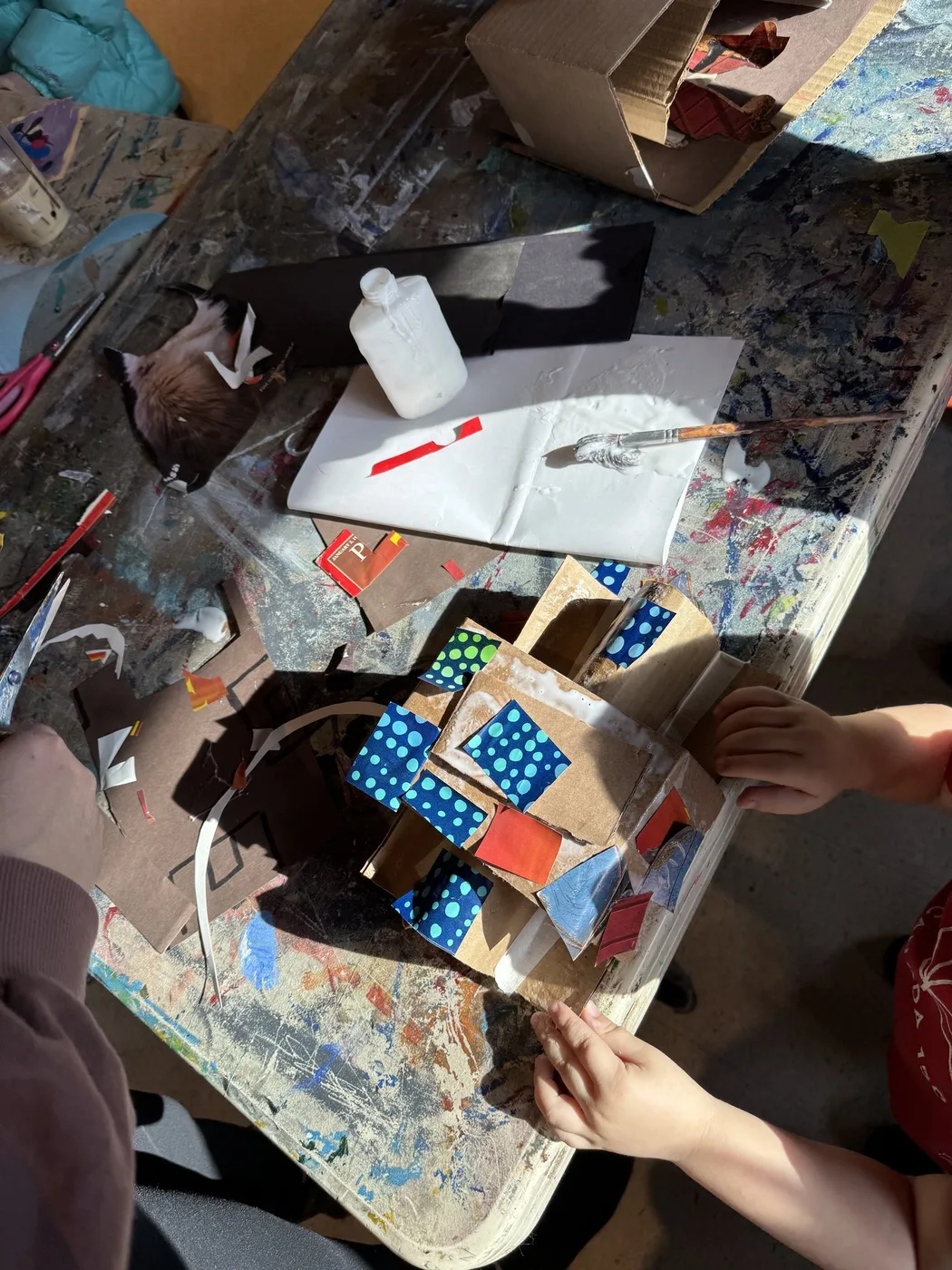 Hands building a painted cardboard house