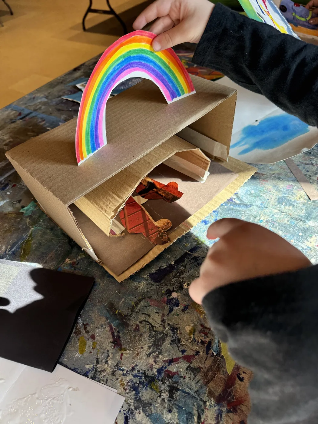 Hand holding a paper rainbow over a cardboard box