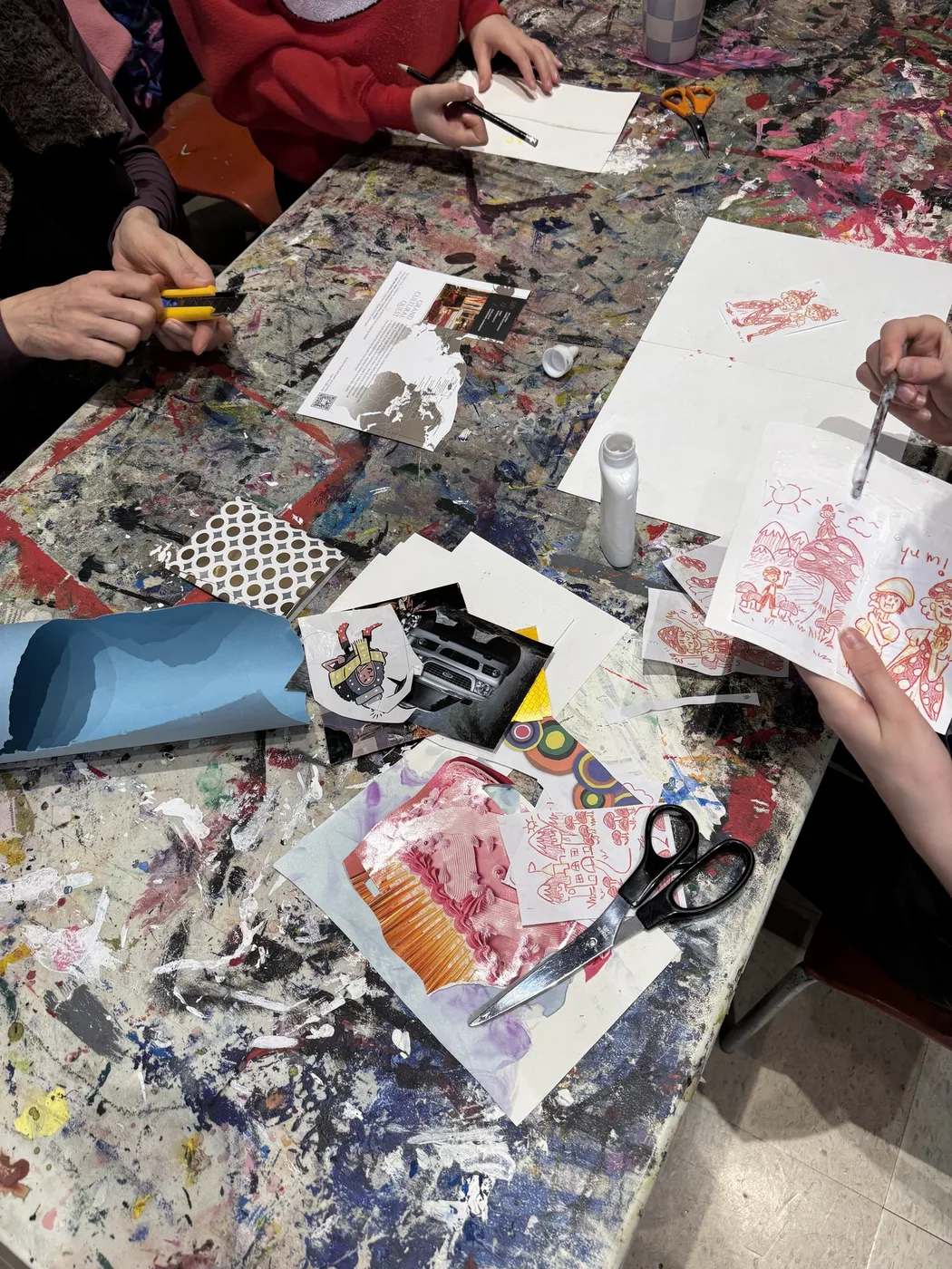 Hands printing and cutting at a crowded art table