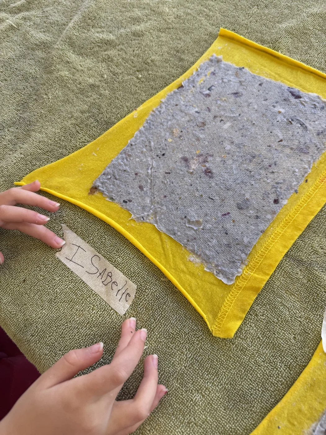 Hands beside a handmade paper sheet with yellow border