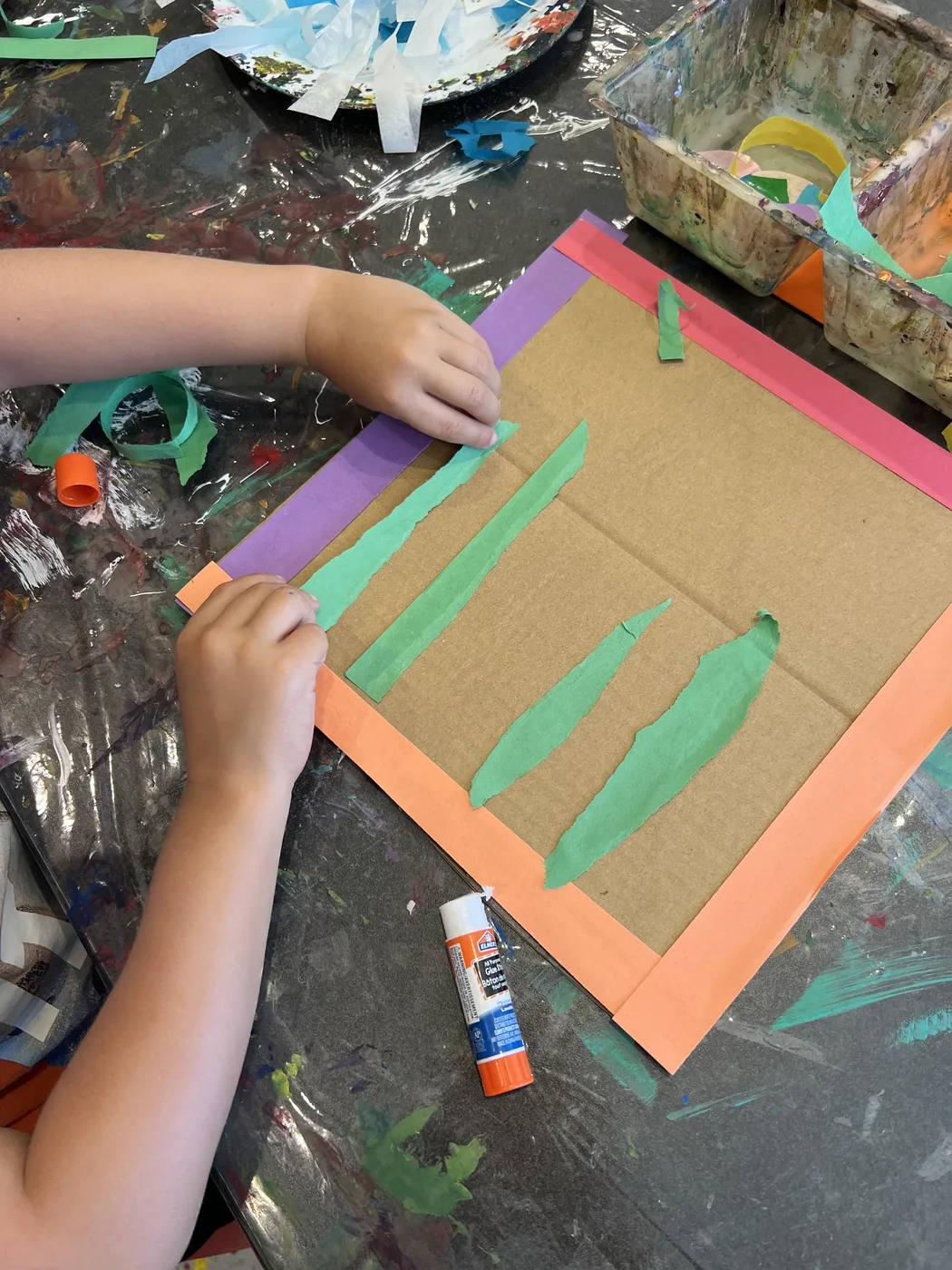 Hands gluing green paper strips onto cardboard