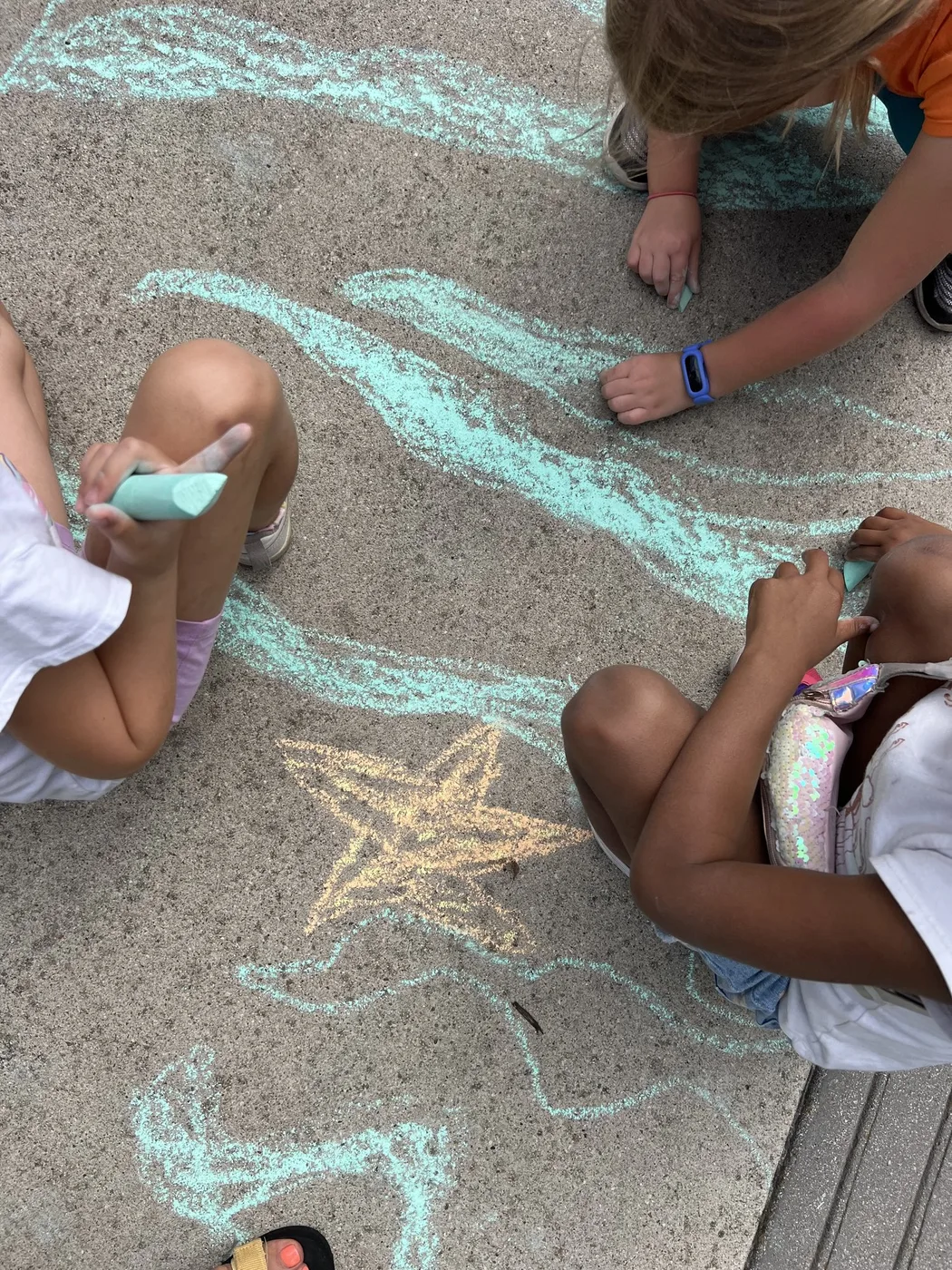 Children’s hands drawing waves and a star in chalk