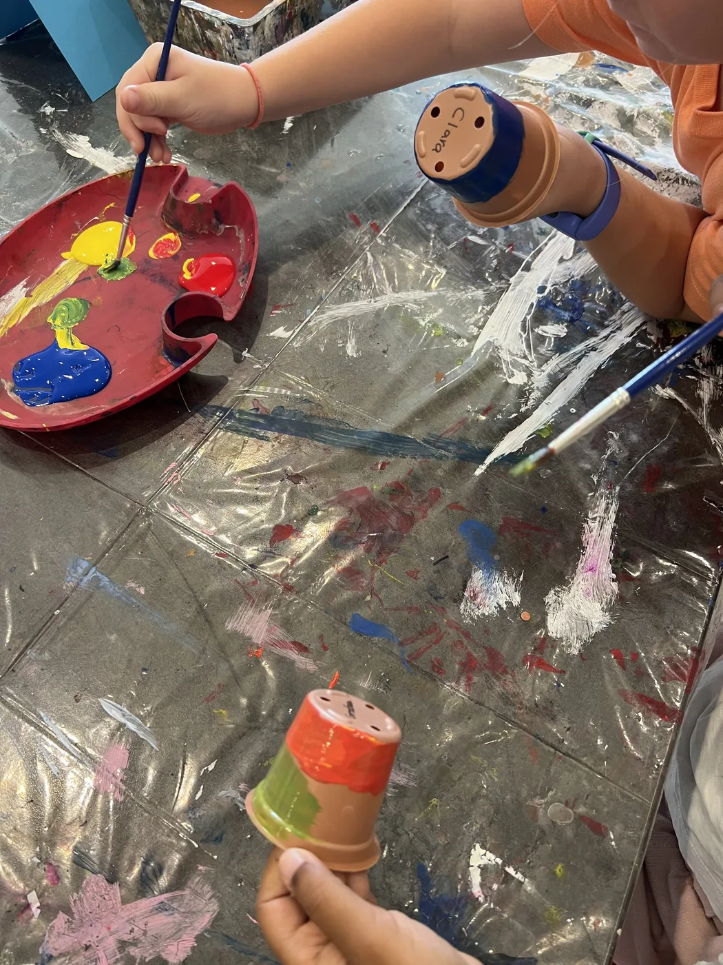 Hands painting clay pots beside a paint palette