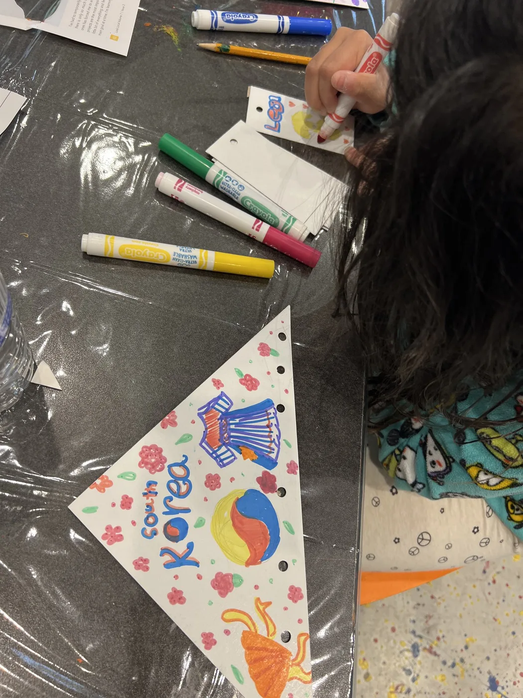 Child colouring a tag beside a Korea pennant