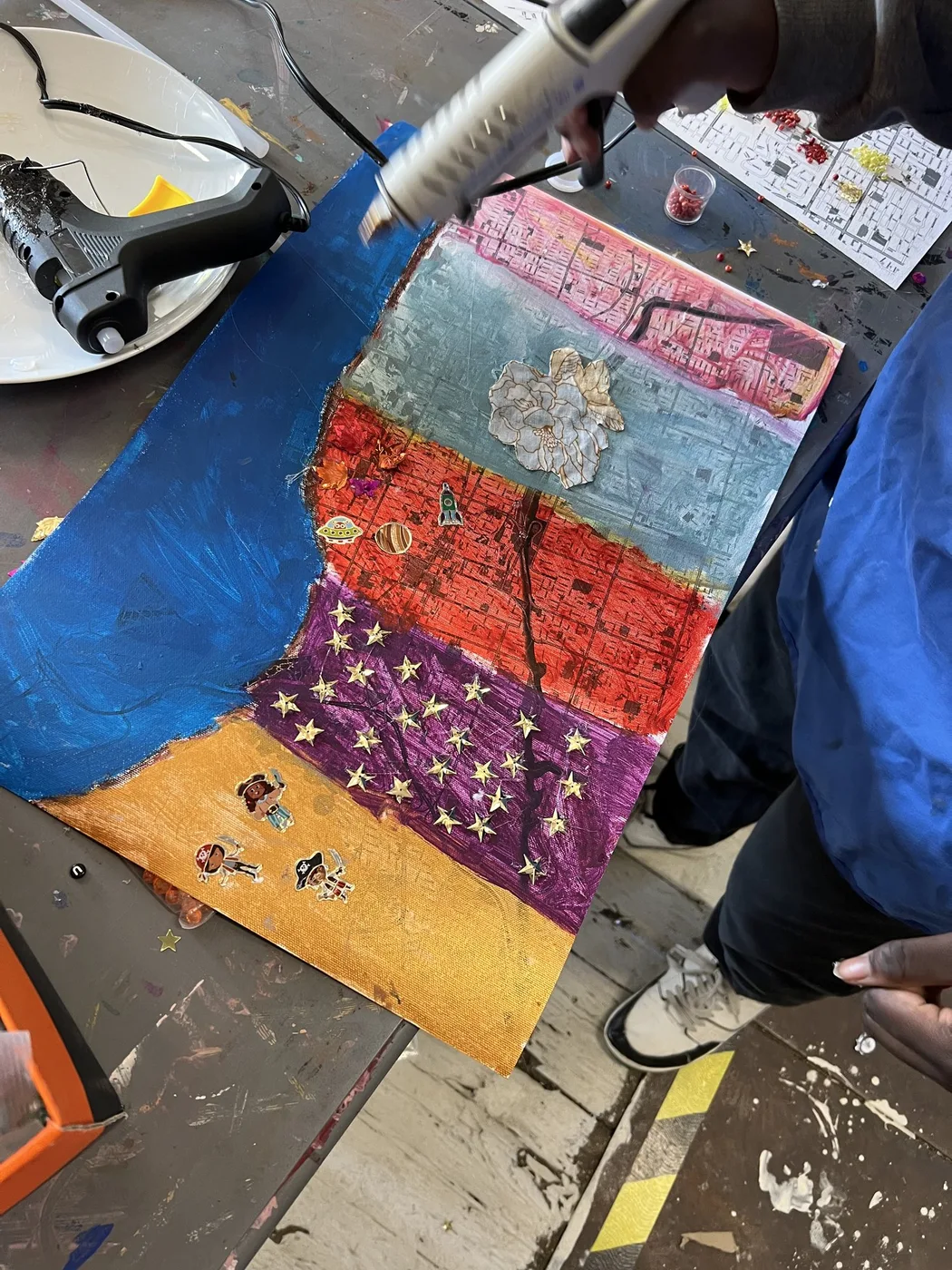 Glue gun over a striped painted map collage
