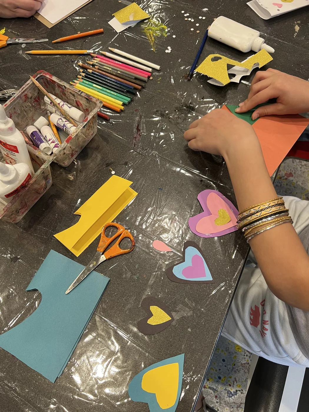 Hands cutting paper hearts at a craft table