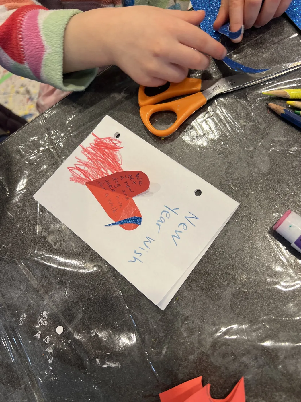 Hands cutting blue glitter beside a heart wish card