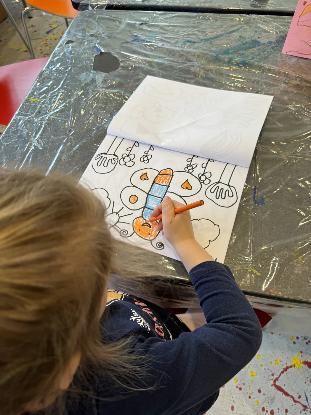 Child colouring a doodle drawing in orange