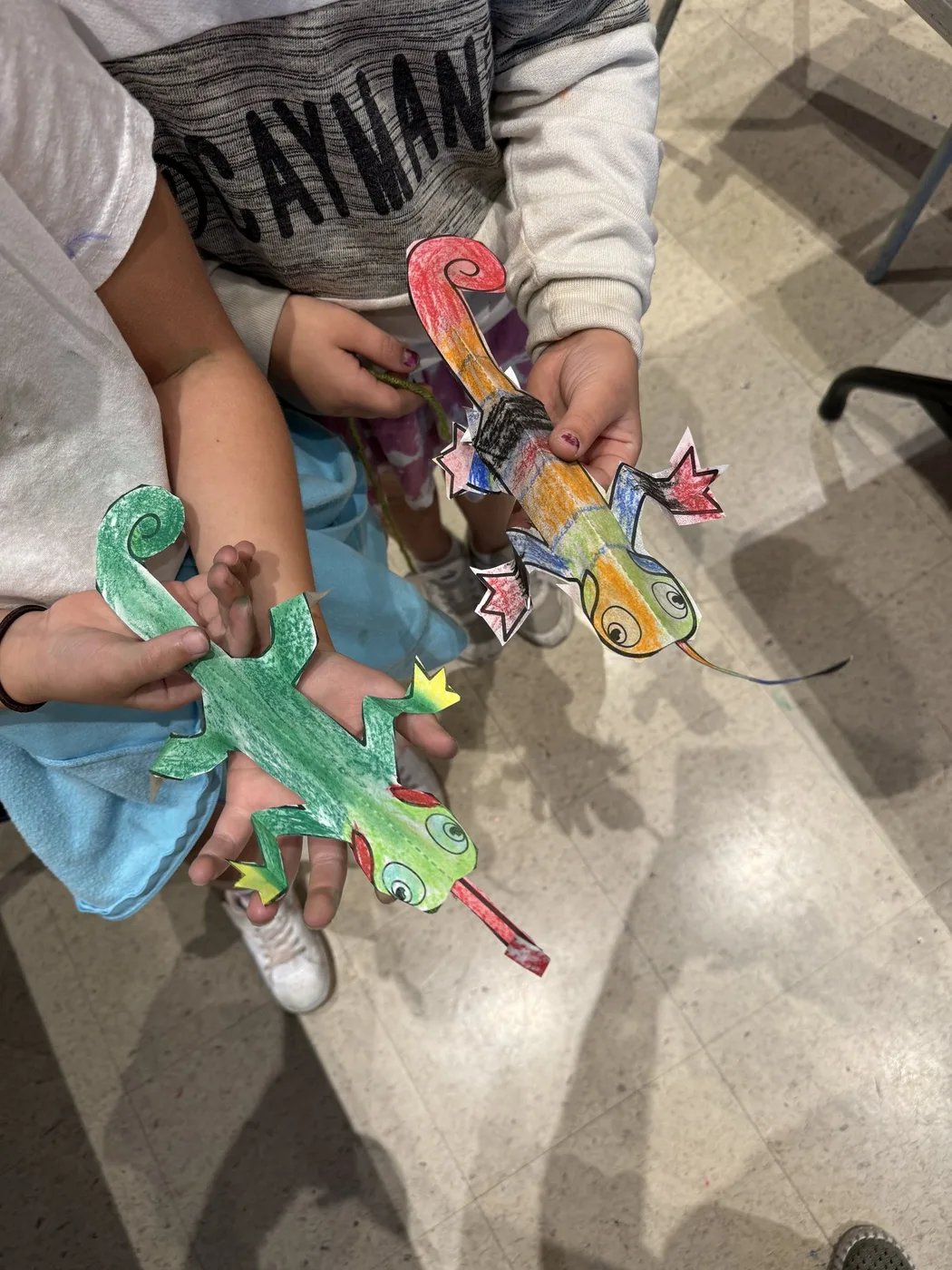 Hands holding two coloured paper lizards