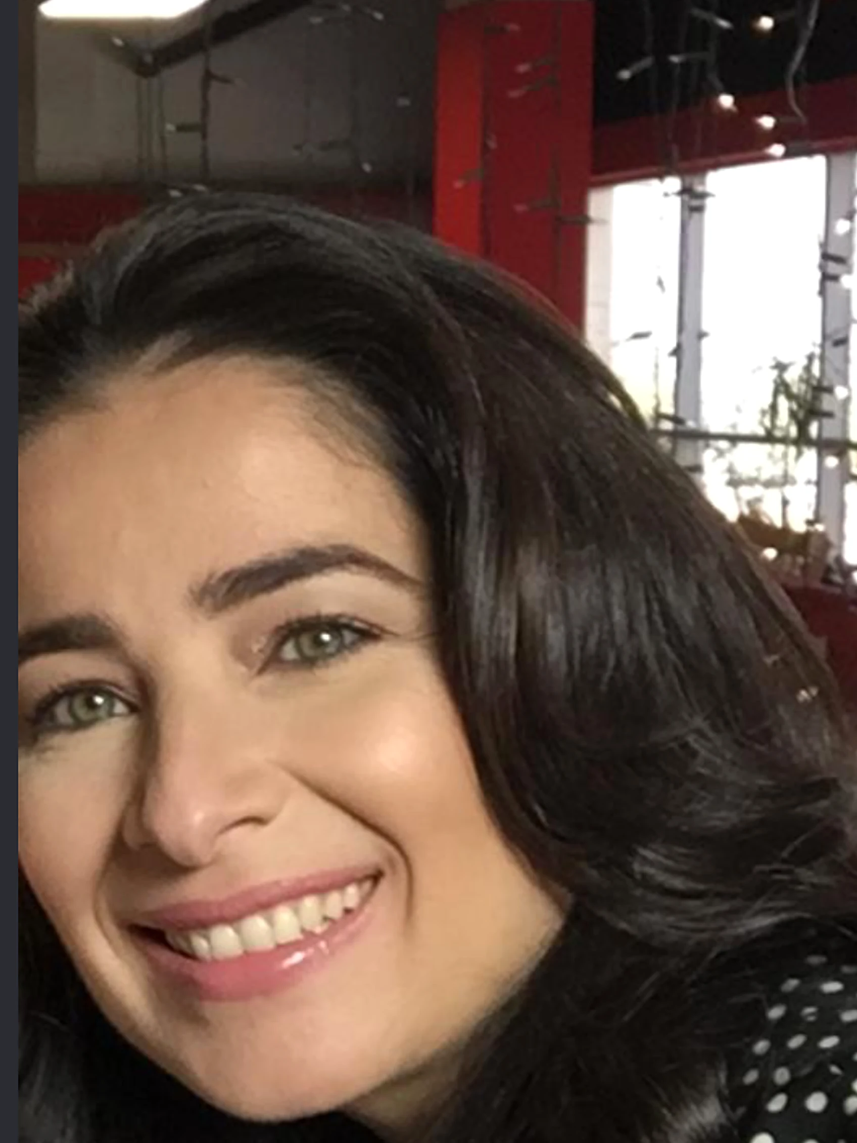 عروب صبح، عن قرب، مبتسمة، بقميص أسود منقّط بالأبيض، وجدران استديو حمراء وأضواء صغيرة خلفها. من تصويرها.
