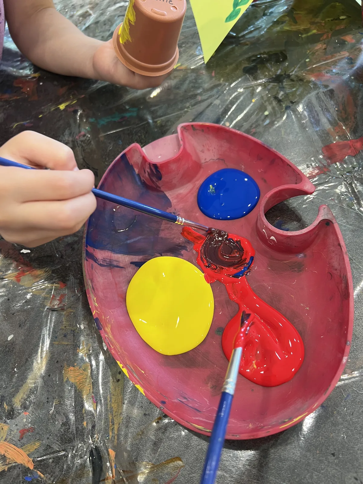 Hands mixing red, yellow and blue paint on a palette