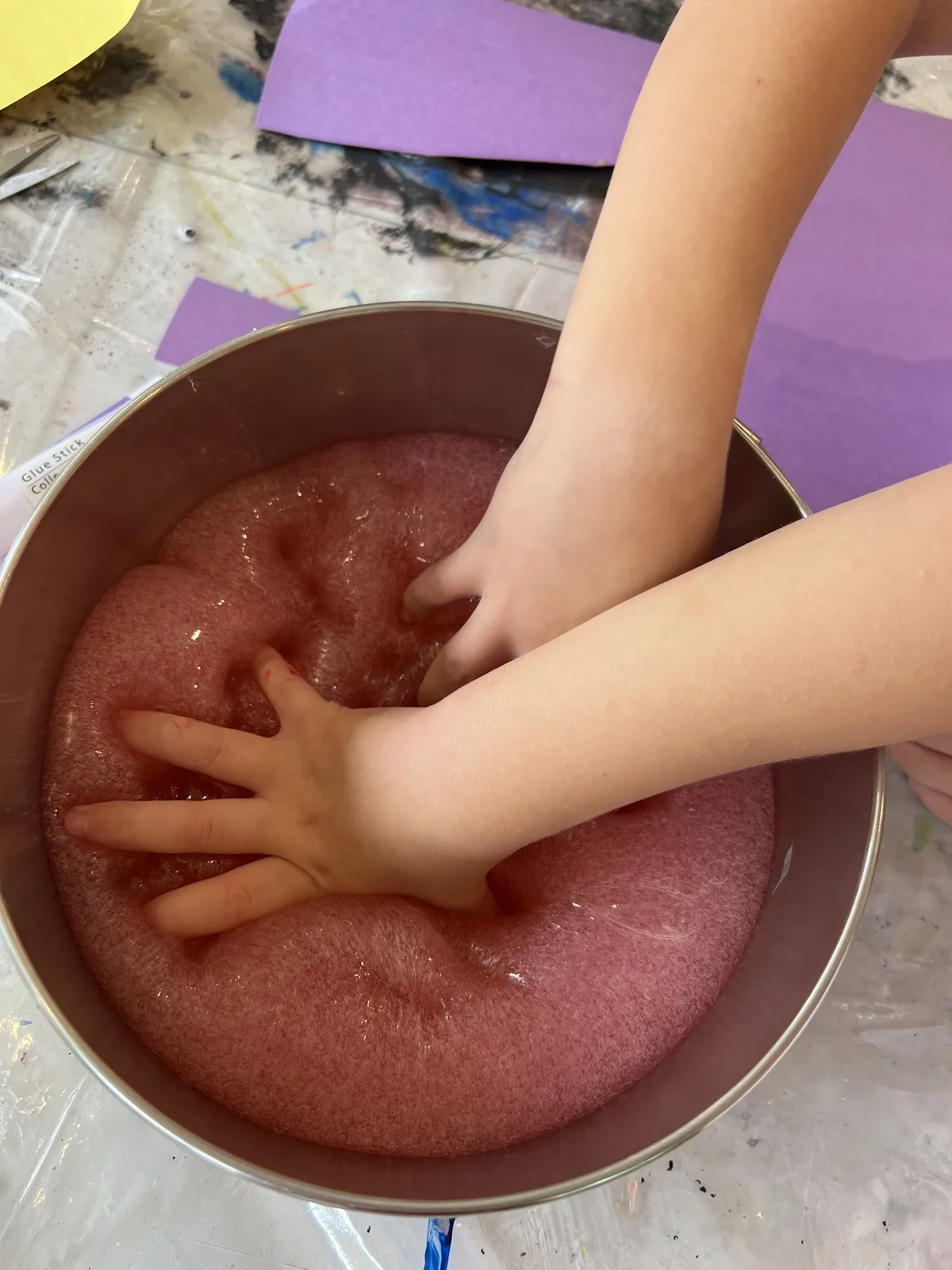 A child's hands pressed into a bowl of pink foam sensory material