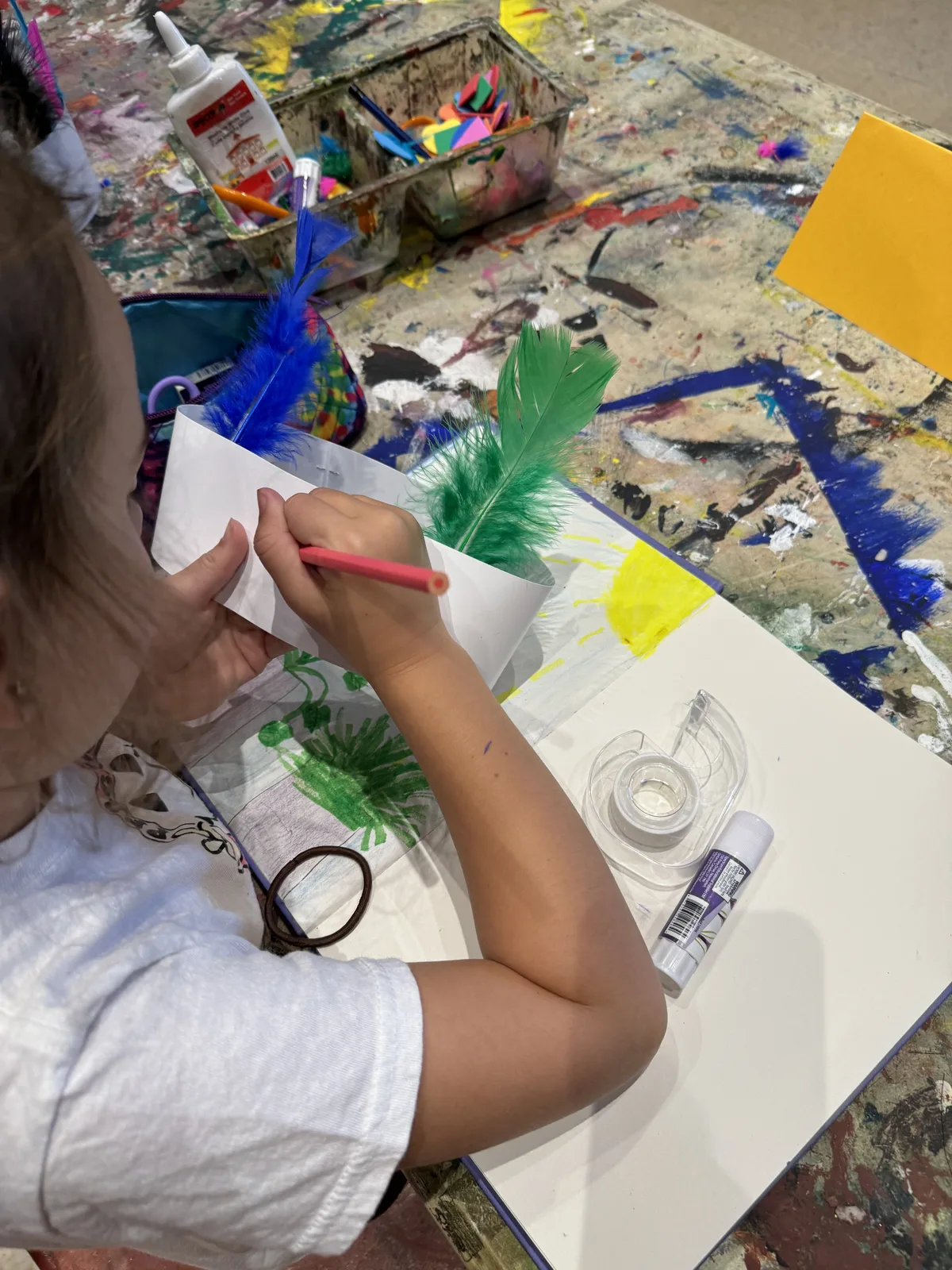 A child's hands gluing colourful feathers onto craft paper