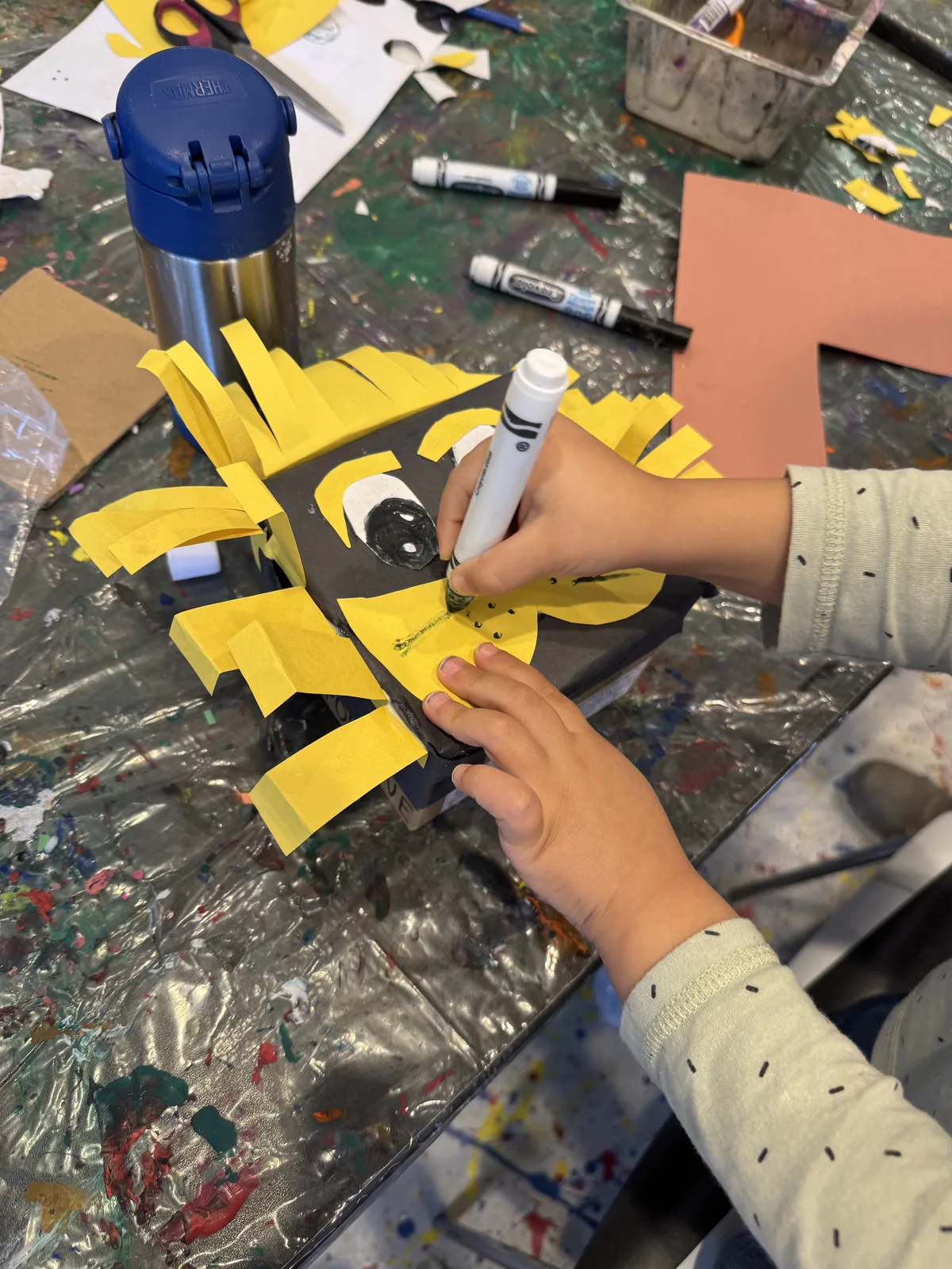 A child's hands adding yellow paper details to a craft figure