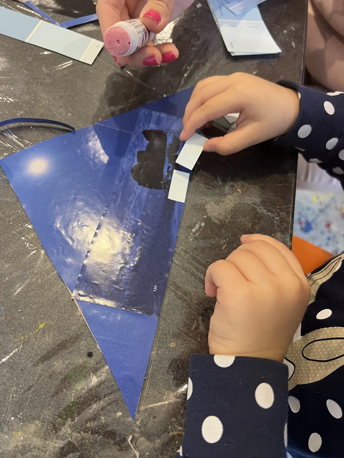 Children's hands attaching blue paper shapes to a craft