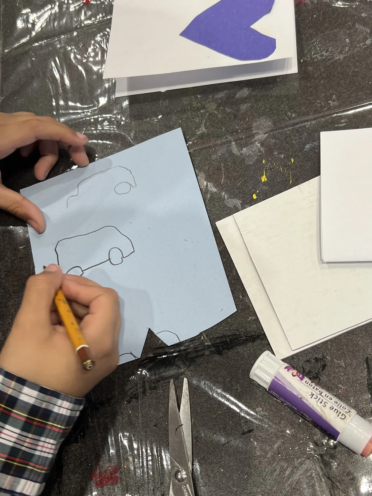 A child's hands sketching a car outline on blue paper