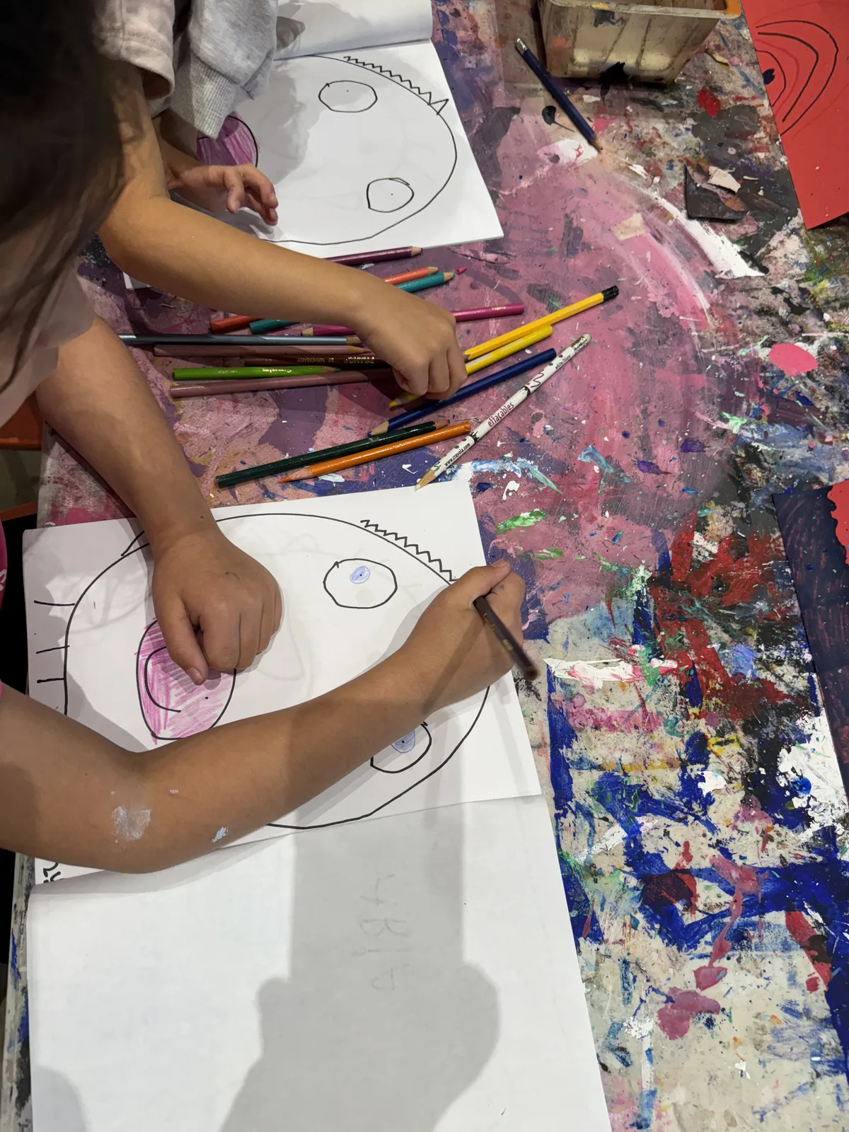 Two children colouring matching face-outline drawings side by side