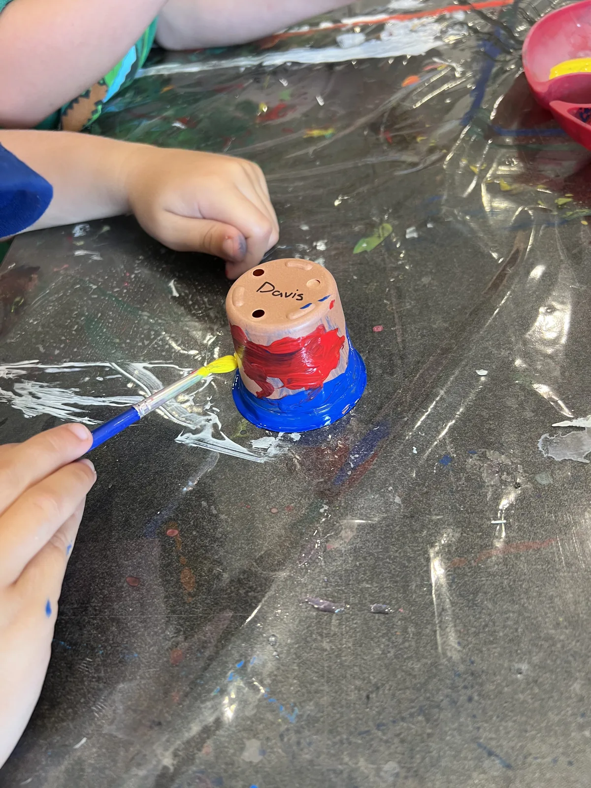 A child's hands painting a small clay pot labelled "Davis"