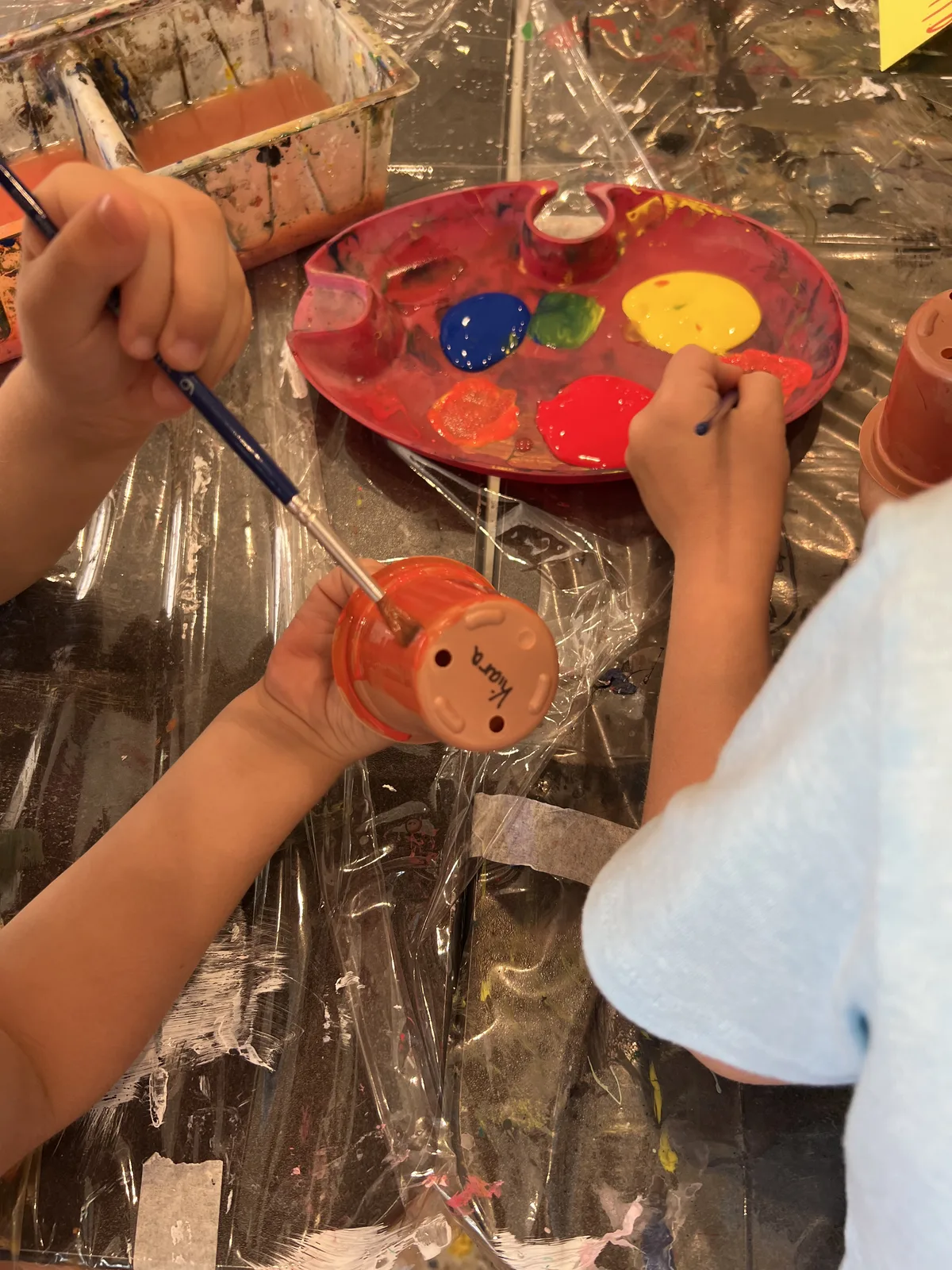 Two children's hands painting clay pots together