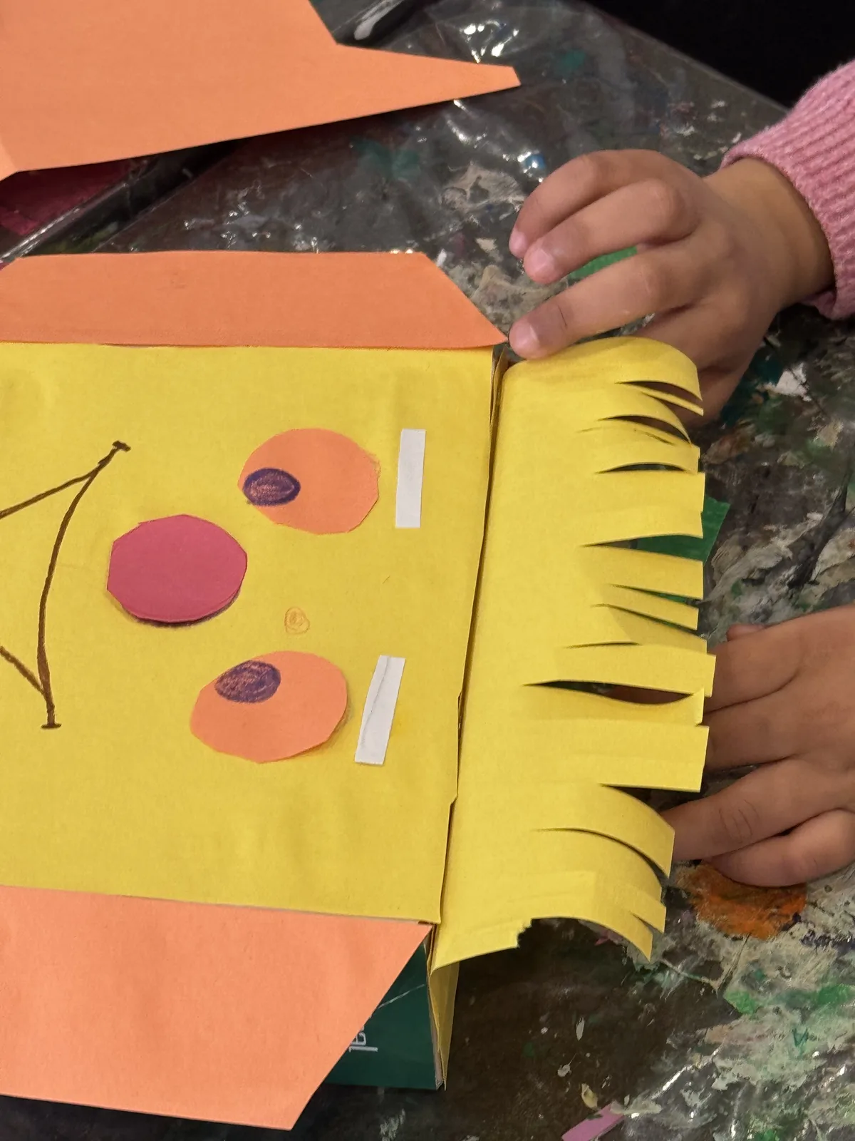 A child's hands assembling a yellow paper craft character