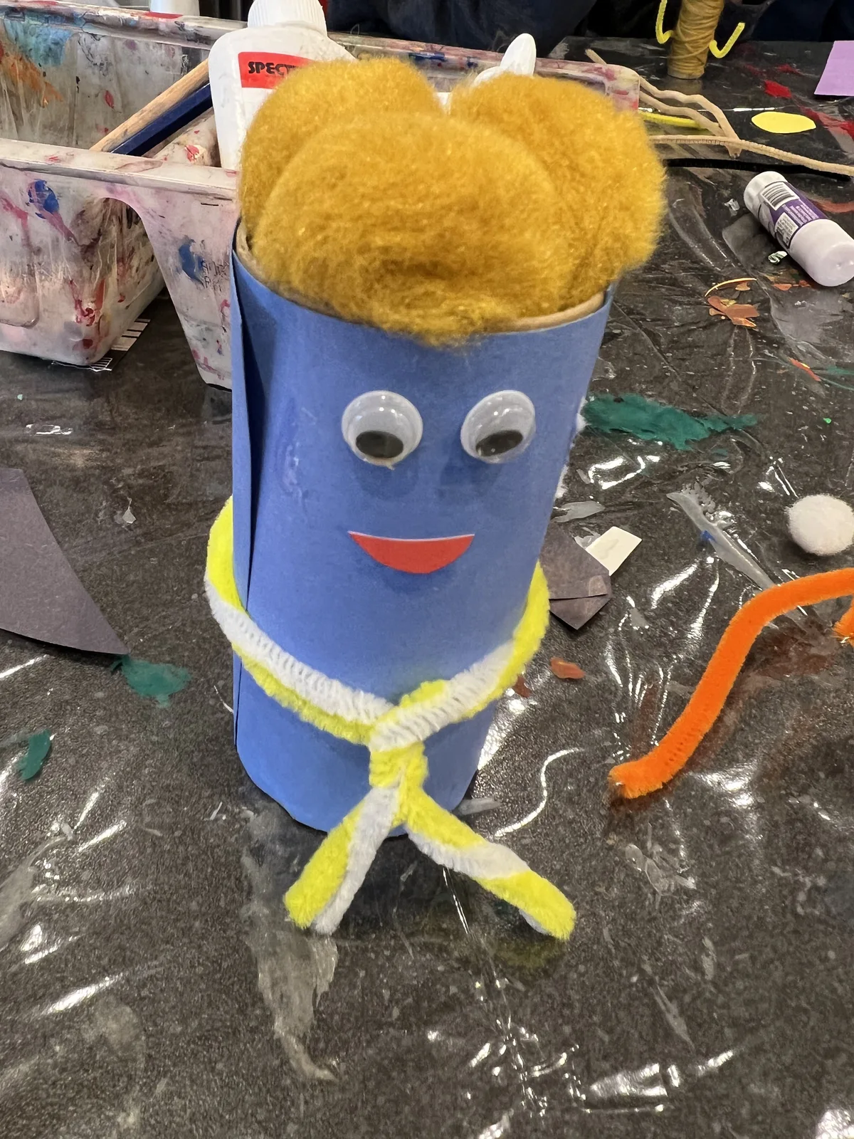 A finished cardboard tube craft figure with googly eyes and a yarn scarf