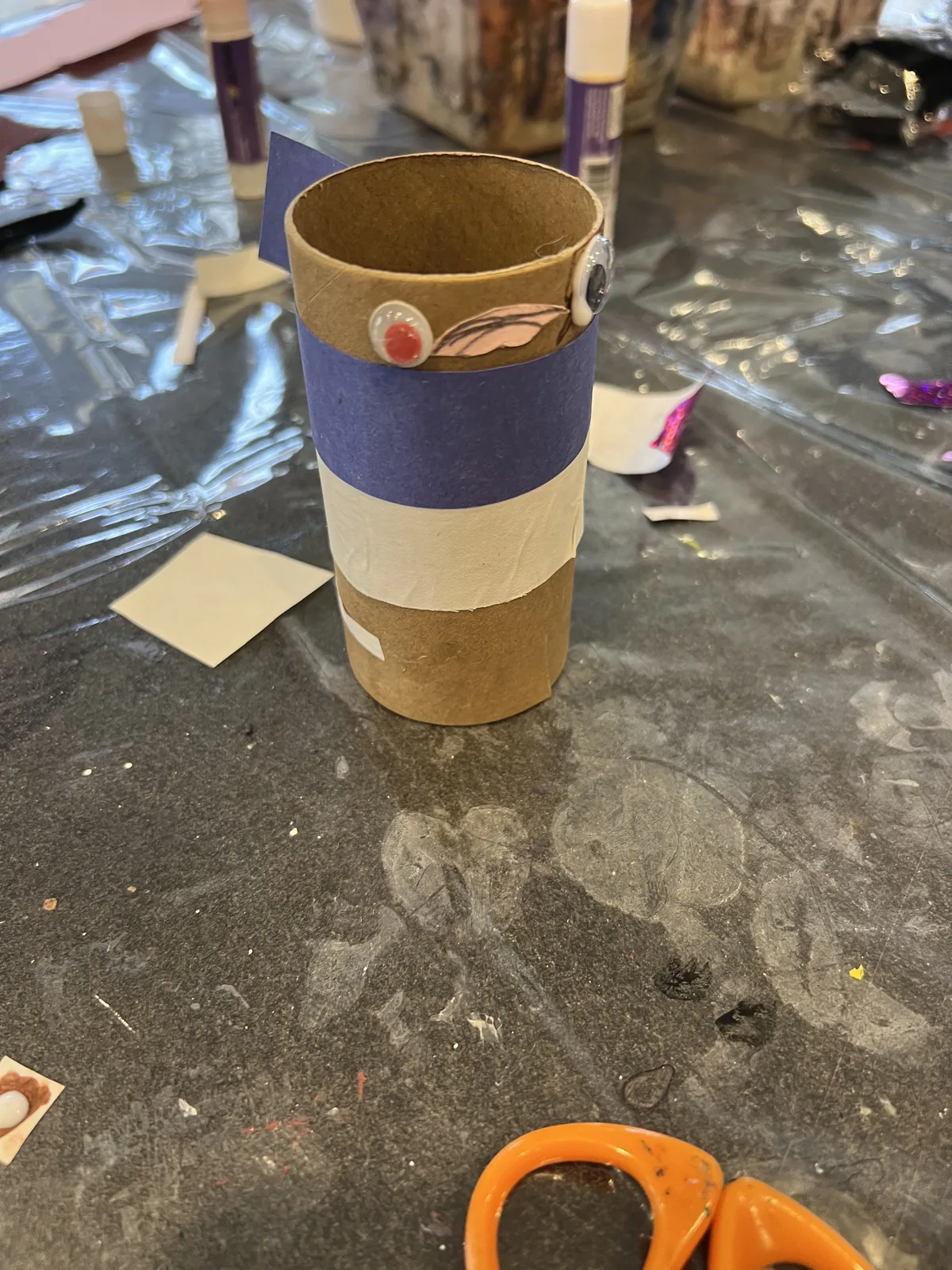A cardboard tube craft with decorative paper bands and eye stickers