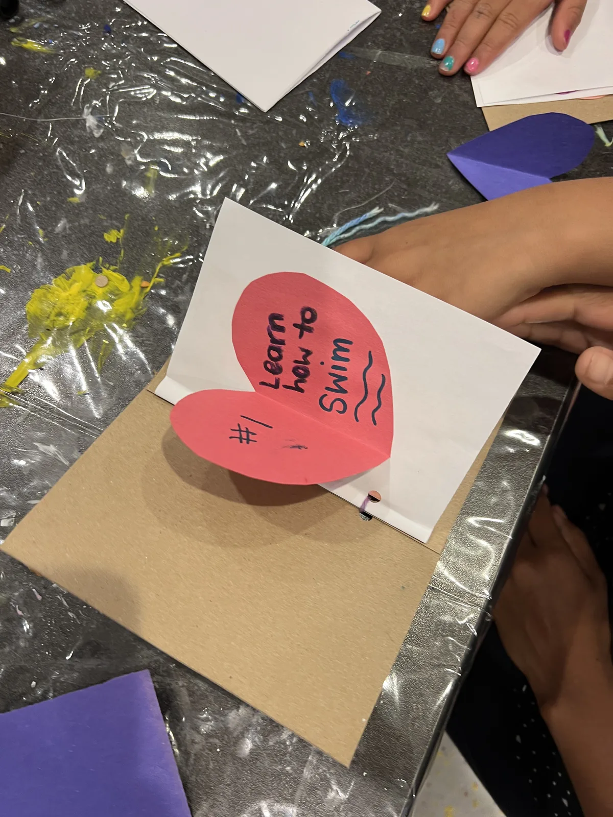 A child's hands assembling a heart-shaped wish card