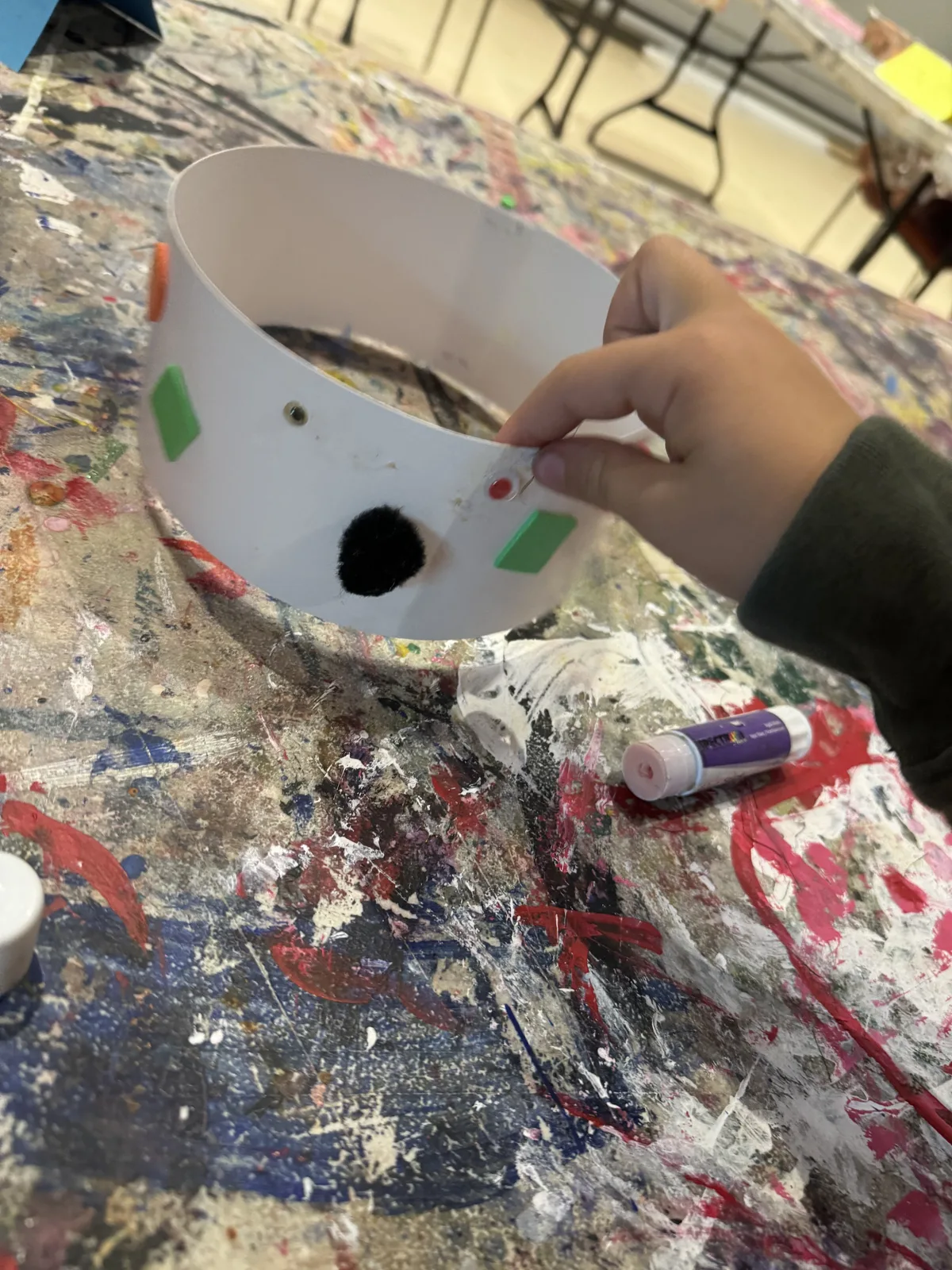 A child's hand decorating a white paper crown craft