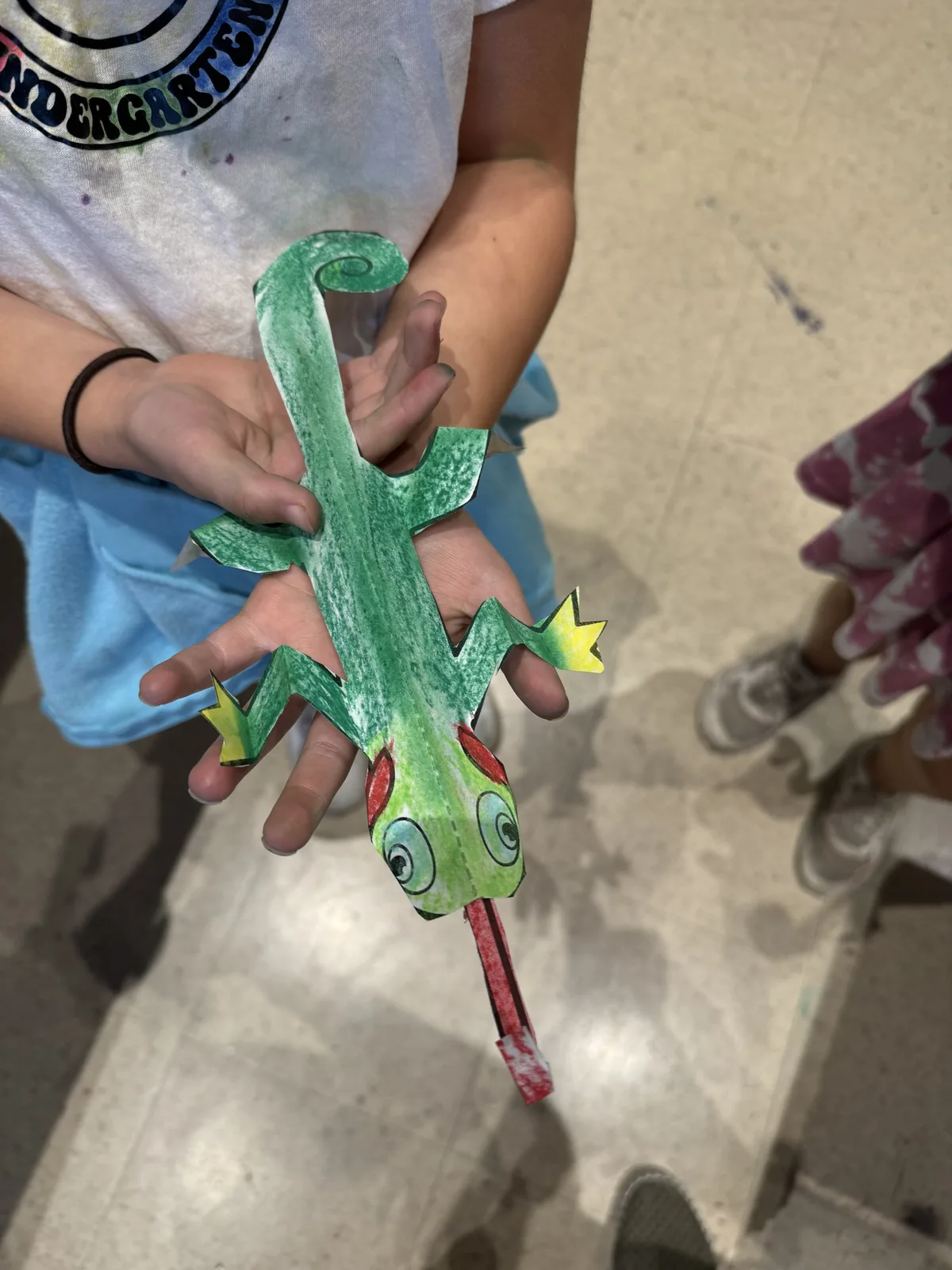 A child's hands holding a hand-painted paper craft lizard