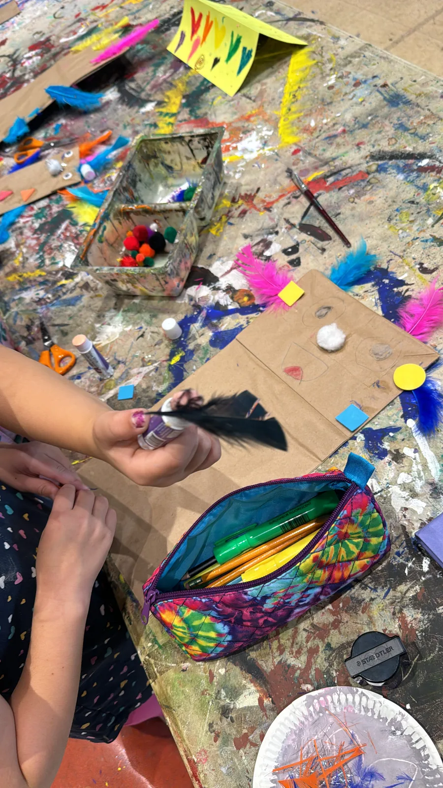 A child's hands arranging feathers and craft supplies on the table