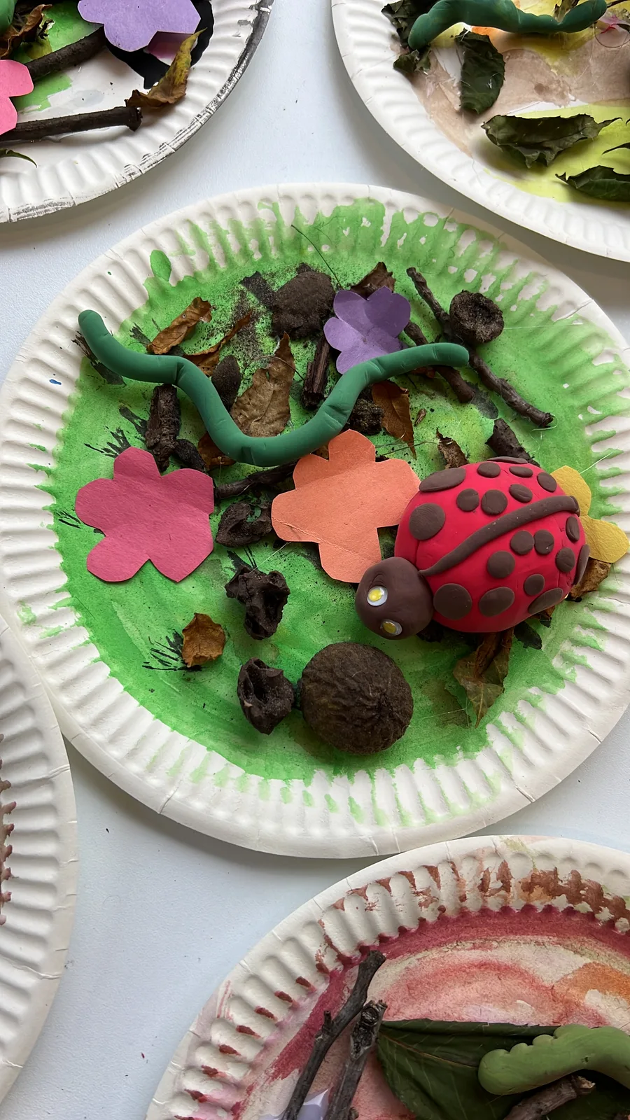 A craft paper plate decorated with a clay ladybug and paper flowers