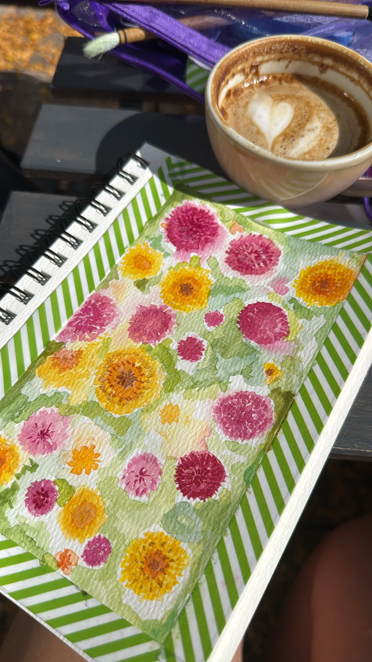 Pink and yellow flower watercolour in a sketchbook beside coffee