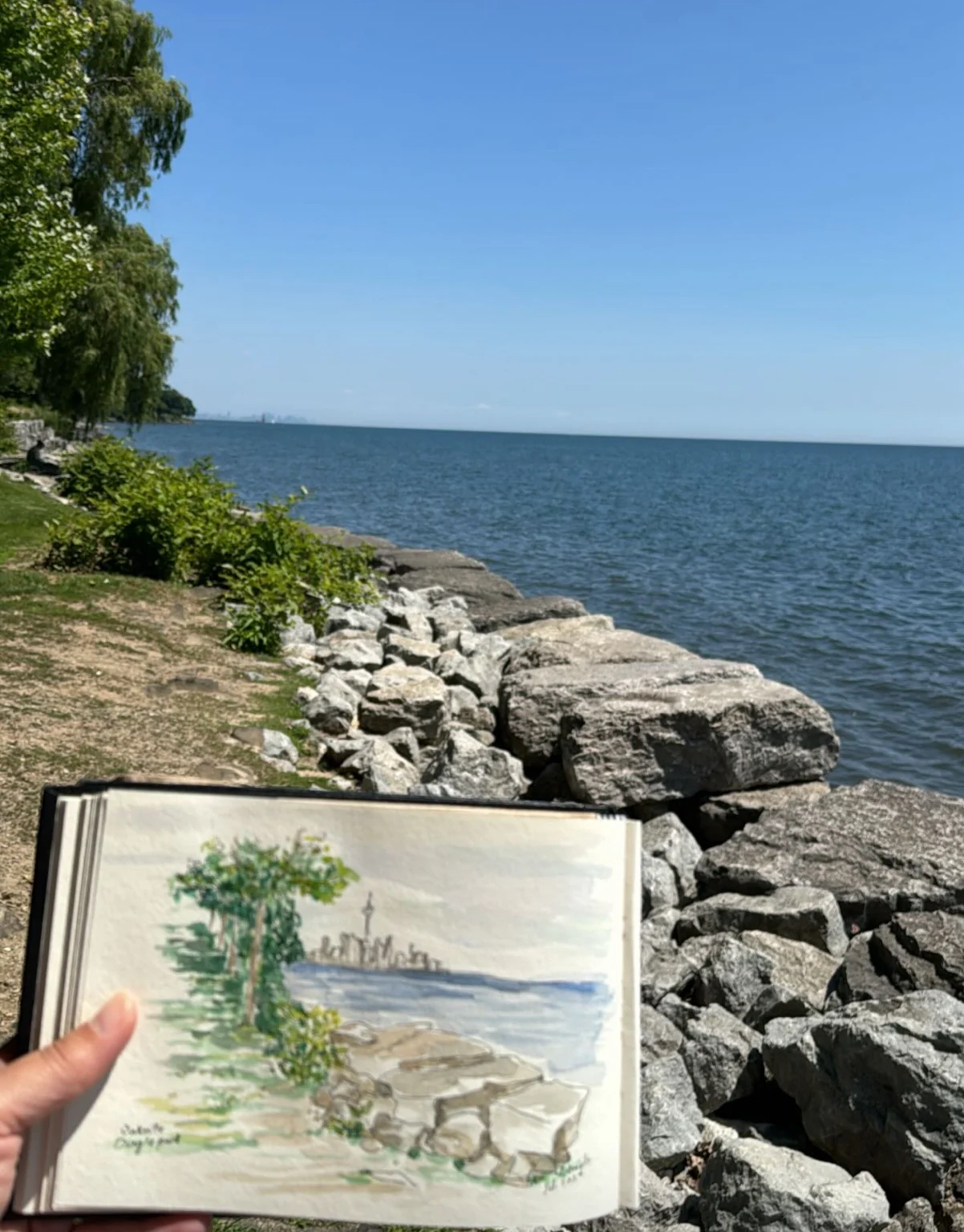 Painted sketchbook beside the rocky lakeshore