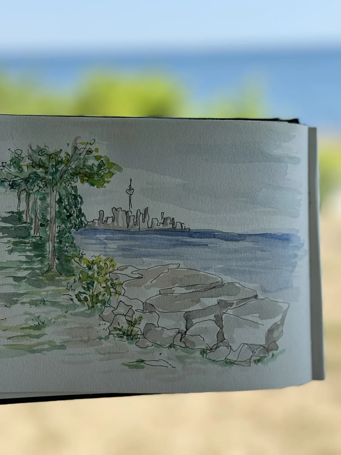 Watercolour sketchbook held beside a lake