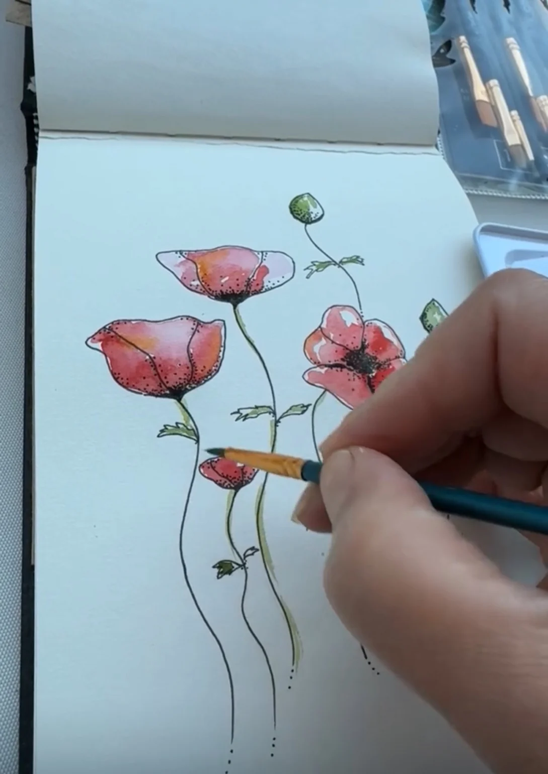 A hand painting red poppies in a sketchbook